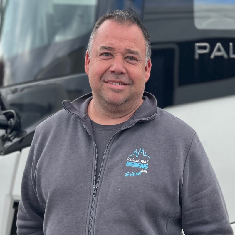 Mann in einem grauen Sweatshirt steht vor einem Fahrzeug mit dem Schriftzug 'Palma'.