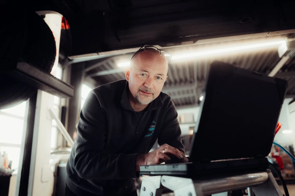 Mann mit Brille arbeitet an einem Laptop in einer Werkstattumgebung.