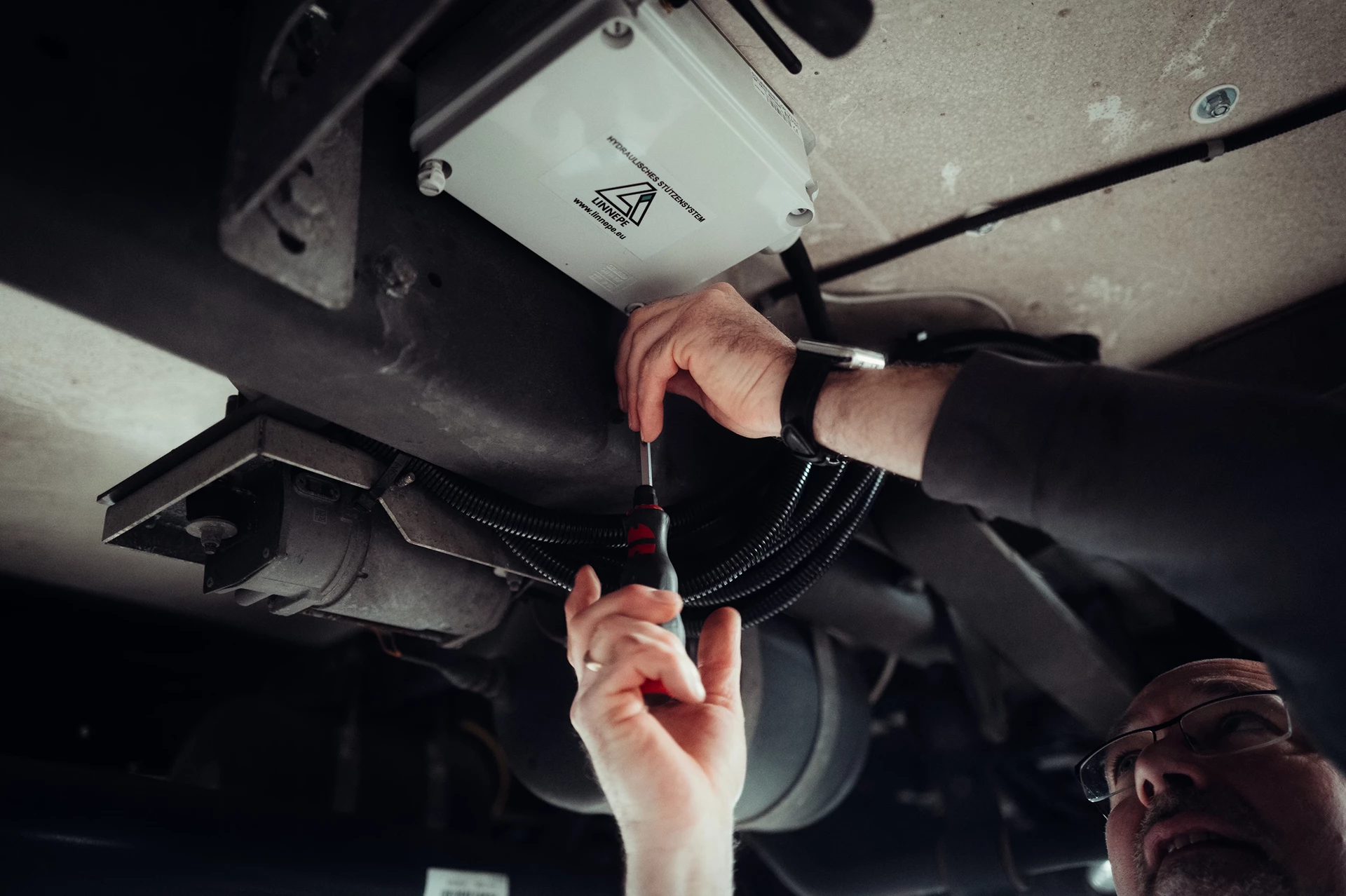 Eine Person, die mit einem Schraubendreher ein Gerät unter einem Fahrzeug installiert.
