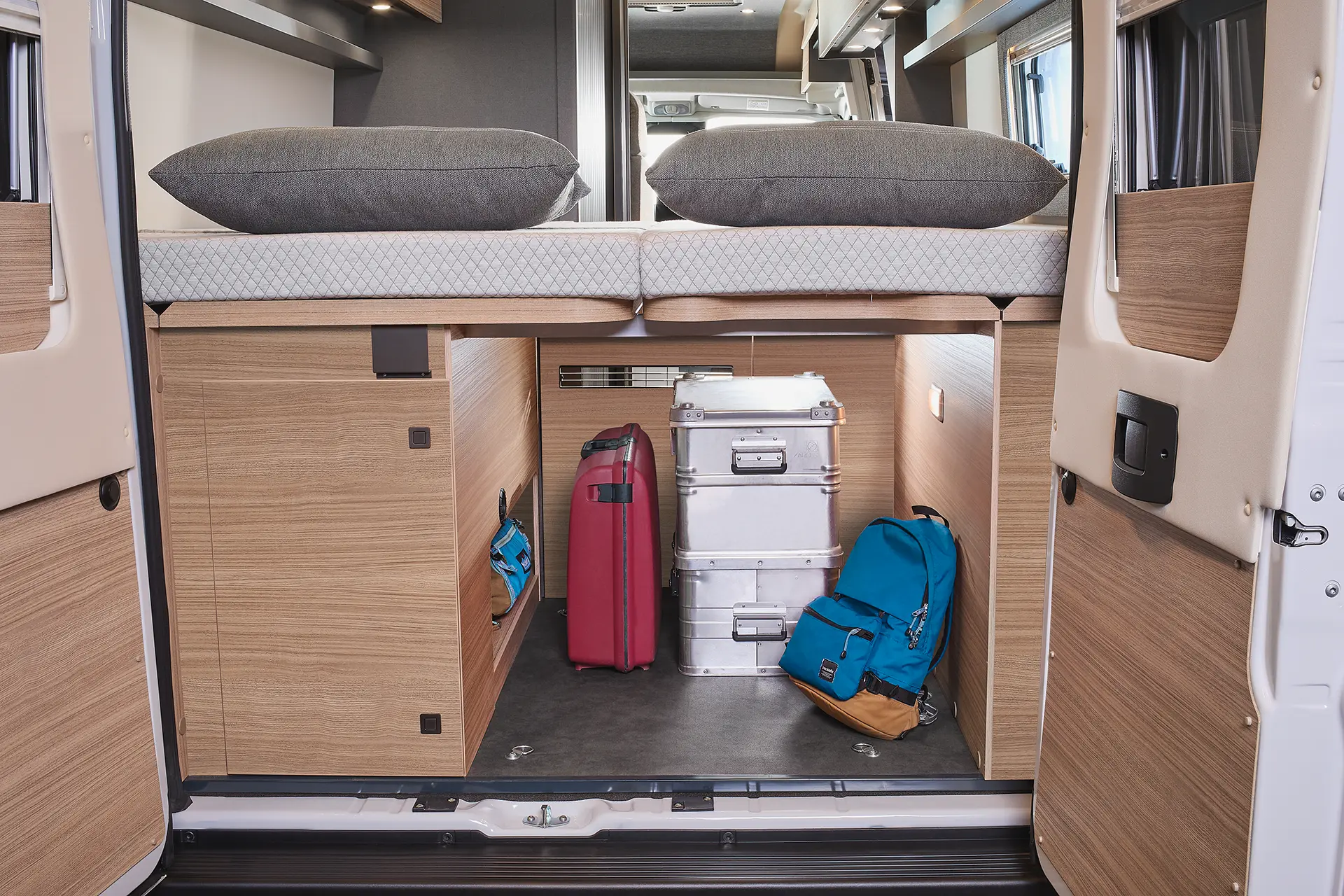 Innenraum eines Wohnmobils mit zwei Koffern und Rucksäcken unter einem Bett.