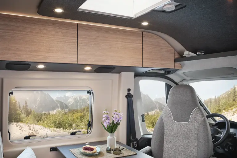 Innenansicht eines Wohnmobils mit Holzregalen und einem Tisch mit Blumen und Gebäck.