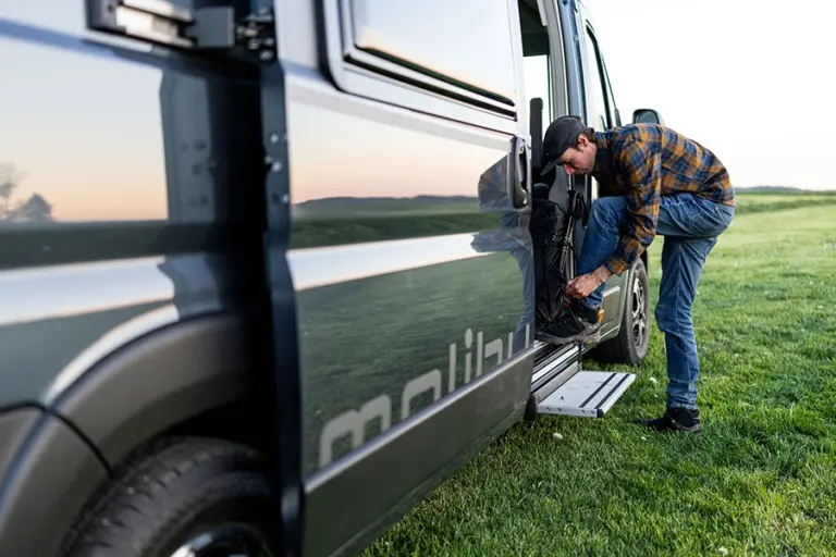 Mann, der seine Schuhe an der offenen Tür eines Wohnmobils anzieht, während er im Freien steht.