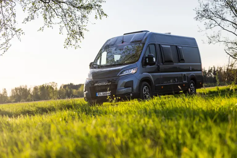 Malibu Relax Camper Van in einer grünen Wiese mit Sonnenlicht im Hintergrund.