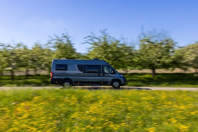 Malibu Relax Wohnmobil fährt auf einer Straße zwischen Bäumen und Wiese.