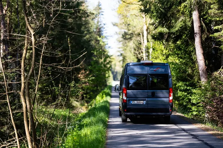 Ein Malibu Fahrzeug fährt auf einer schmalen Waldstraße zwischen Bäumen.