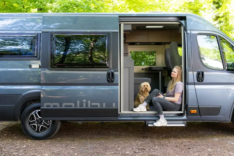 Malibu Relax Van mit geöffneter Schiebetür und Person mit Hund im Innenraum.