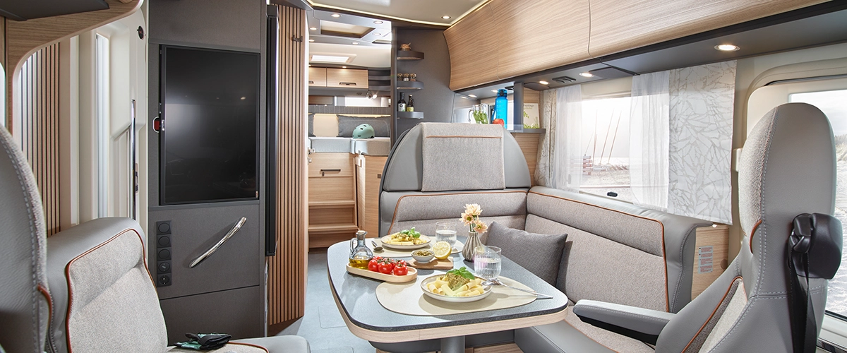 Essbereich im Innenraum eines Reisemobils mit Tisch, Stühlen und gedecktem Tisch.